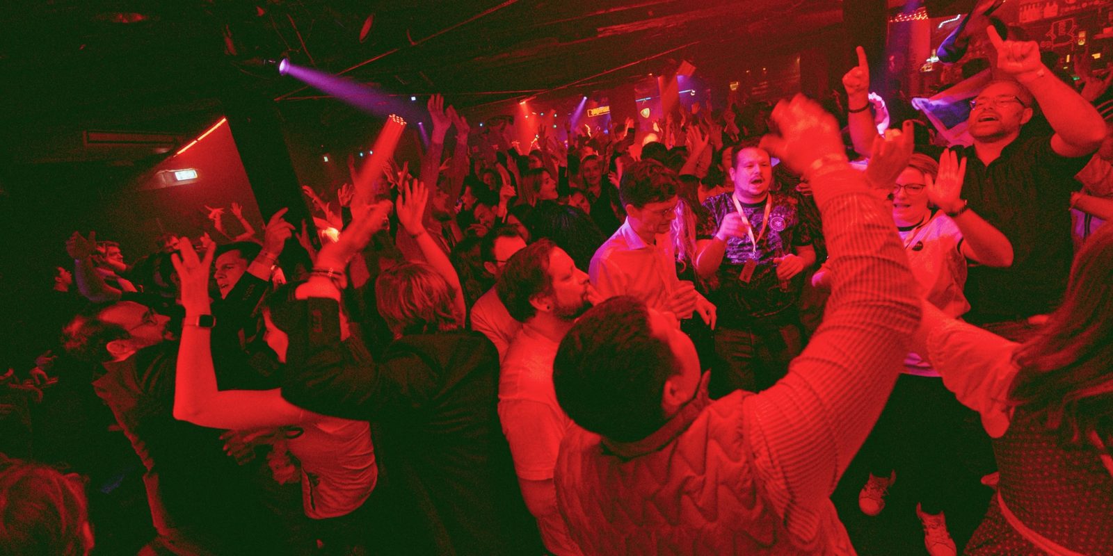 Packed dance floor with red lights and hands in the air